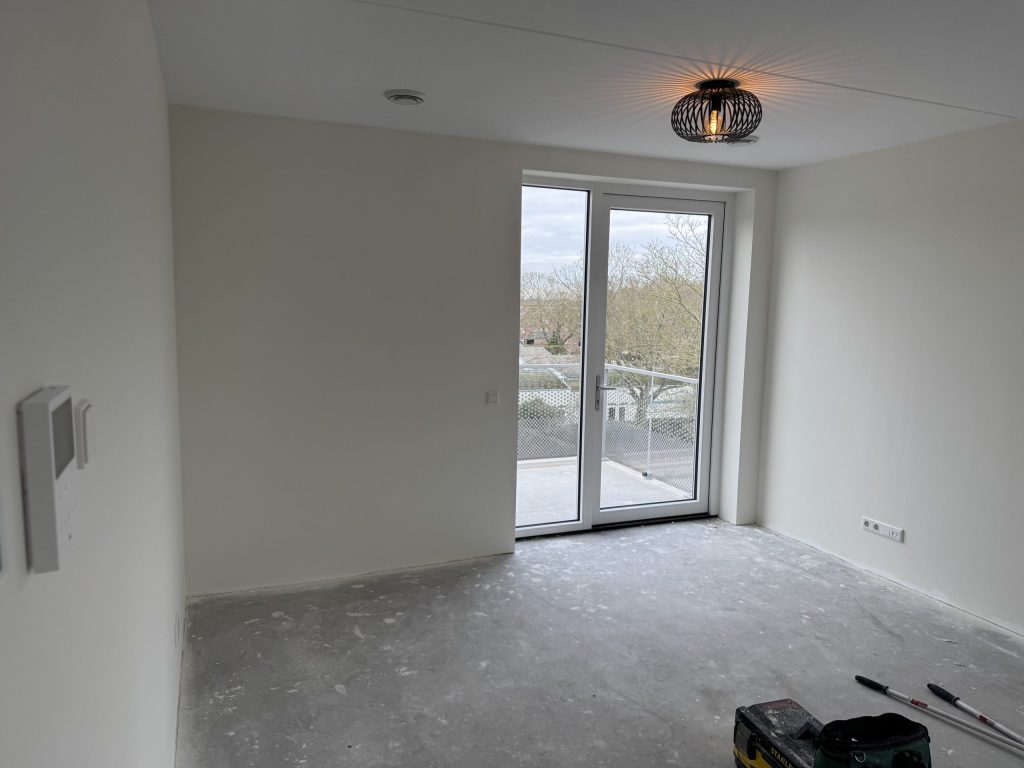 Lege kamer in een nieuw appartement met balkondeur en egale witte wanden, kort na de oplevering